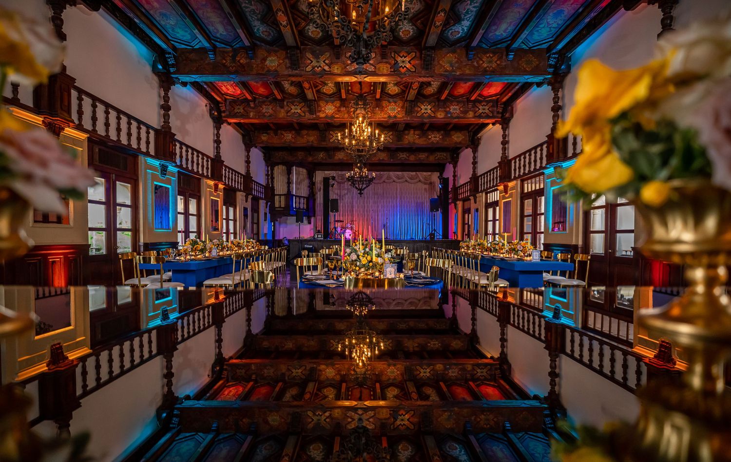 Elegant wedding reception venue with dramatic blue lighting and ornate ceiling details.