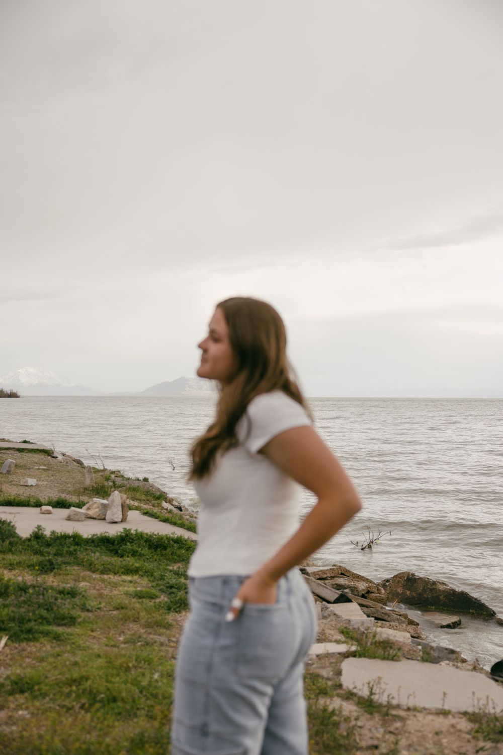 Person in white tee and jeans gazing at ocean view from rocky coastline.