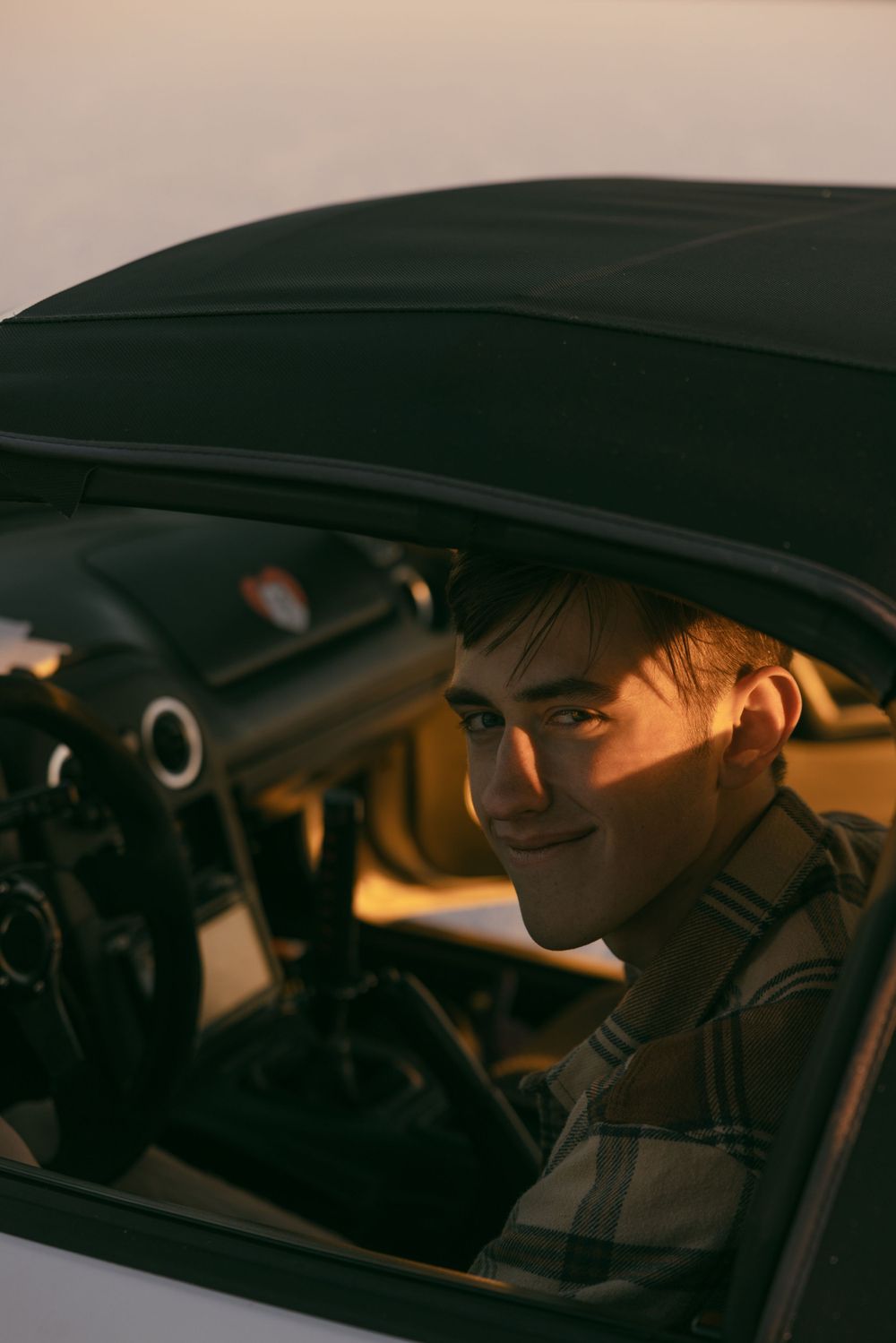 Person smiling behind steering wheel of car at sunset.
