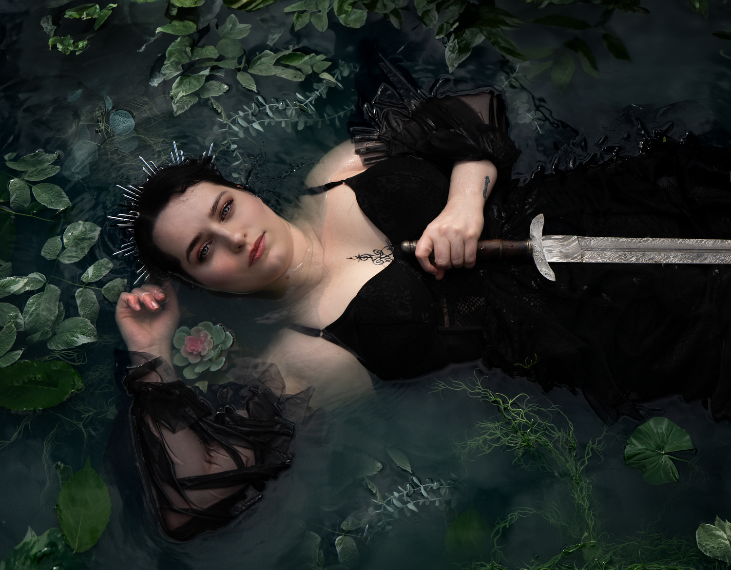 Woman submerged in a pond in a black gown with a sword