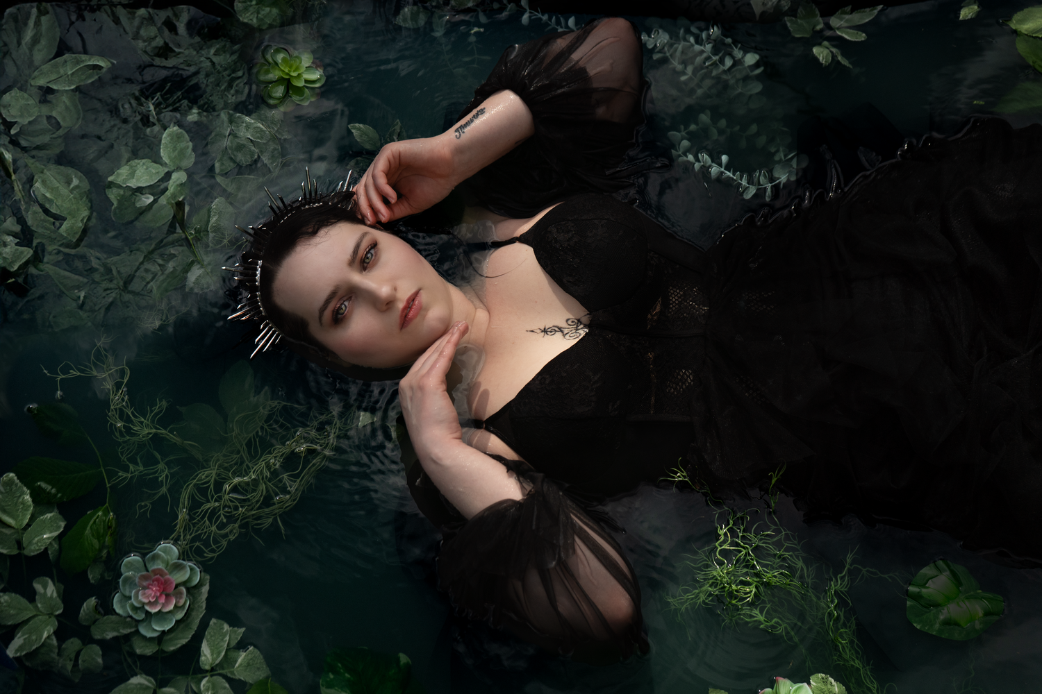 Goth crowned woman submerged in a pond like the Lady of the Lake