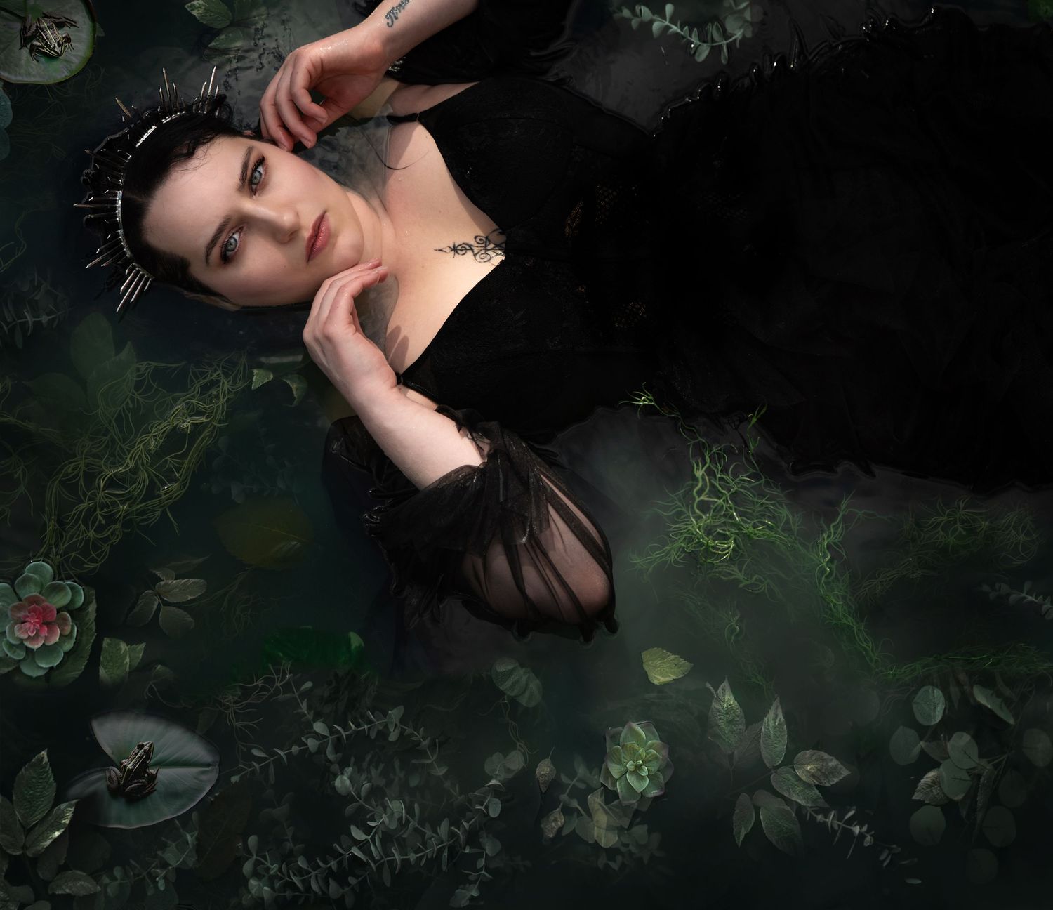 Goth crowned woman submerged in a pond like Ophelia. Lily pads surround her