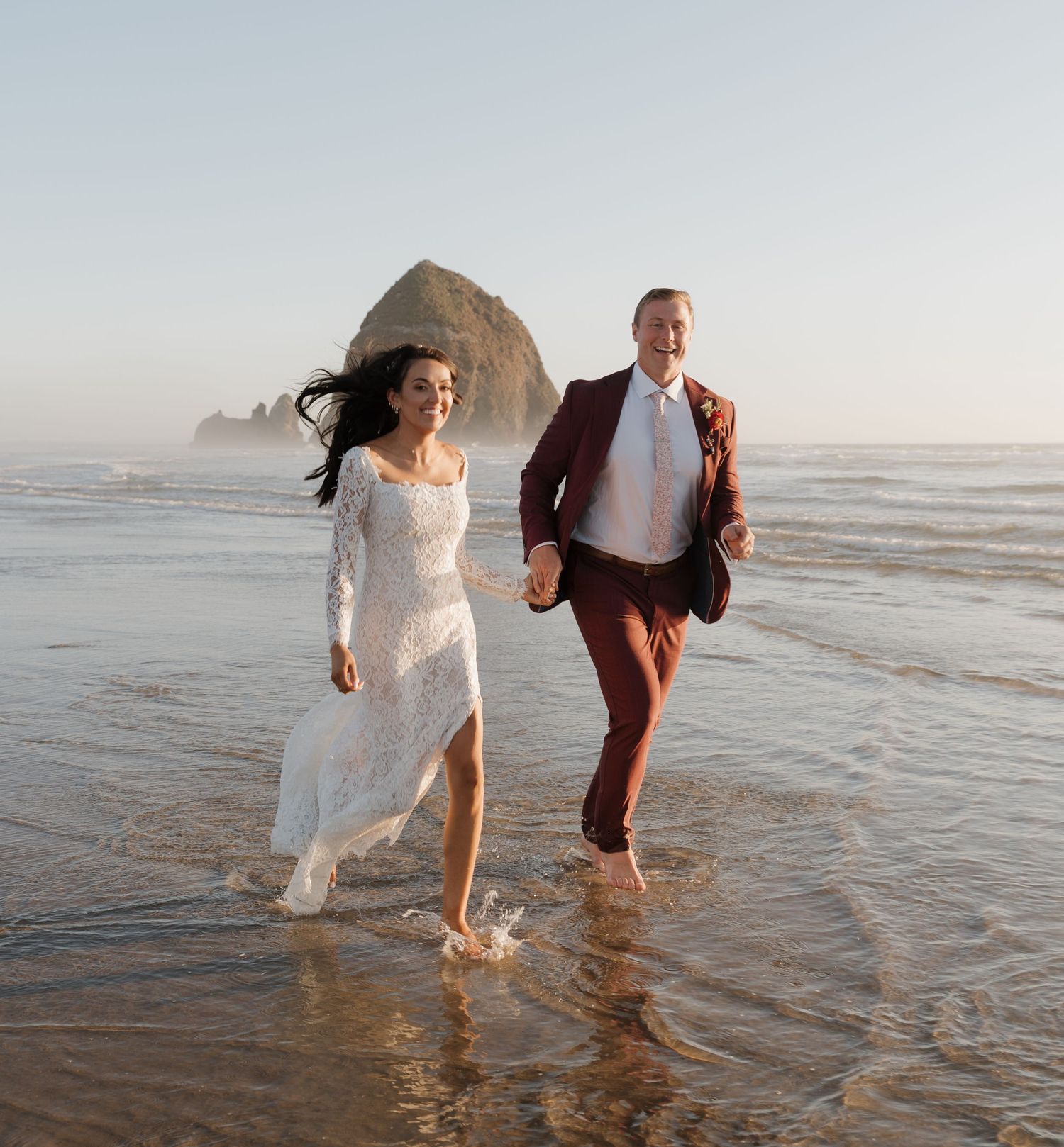 A couple runs playfully through ocean waves at sunset near Haystack Rock.
