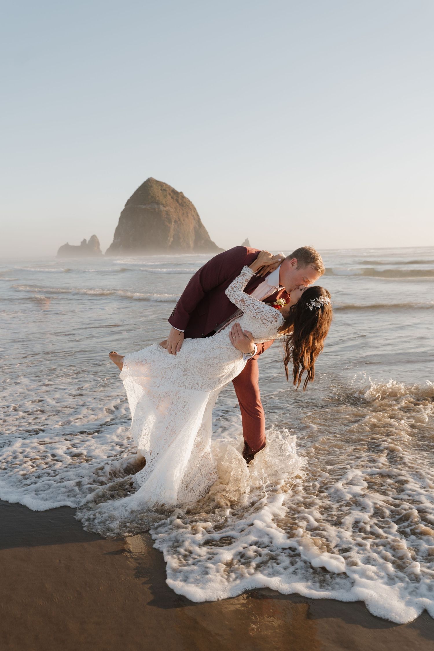 A romantic dip pose on the beach with waves crashing and Haystack Rock in background.
