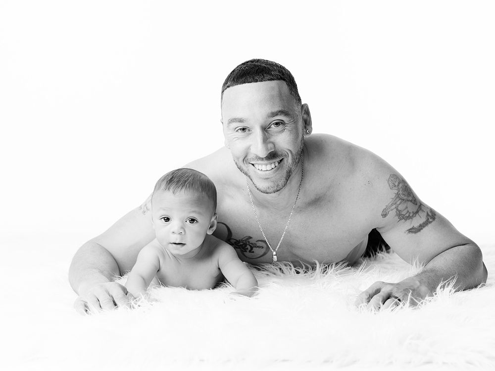 A black and white portrait shows a parent and baby laying on a soft fluffy rug together.