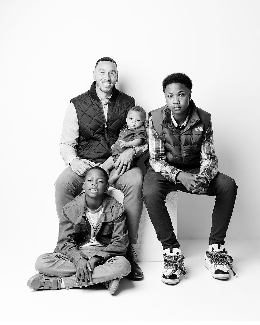 A black and white studio portrait of a family group of four dressed in casual attire against a plain background.