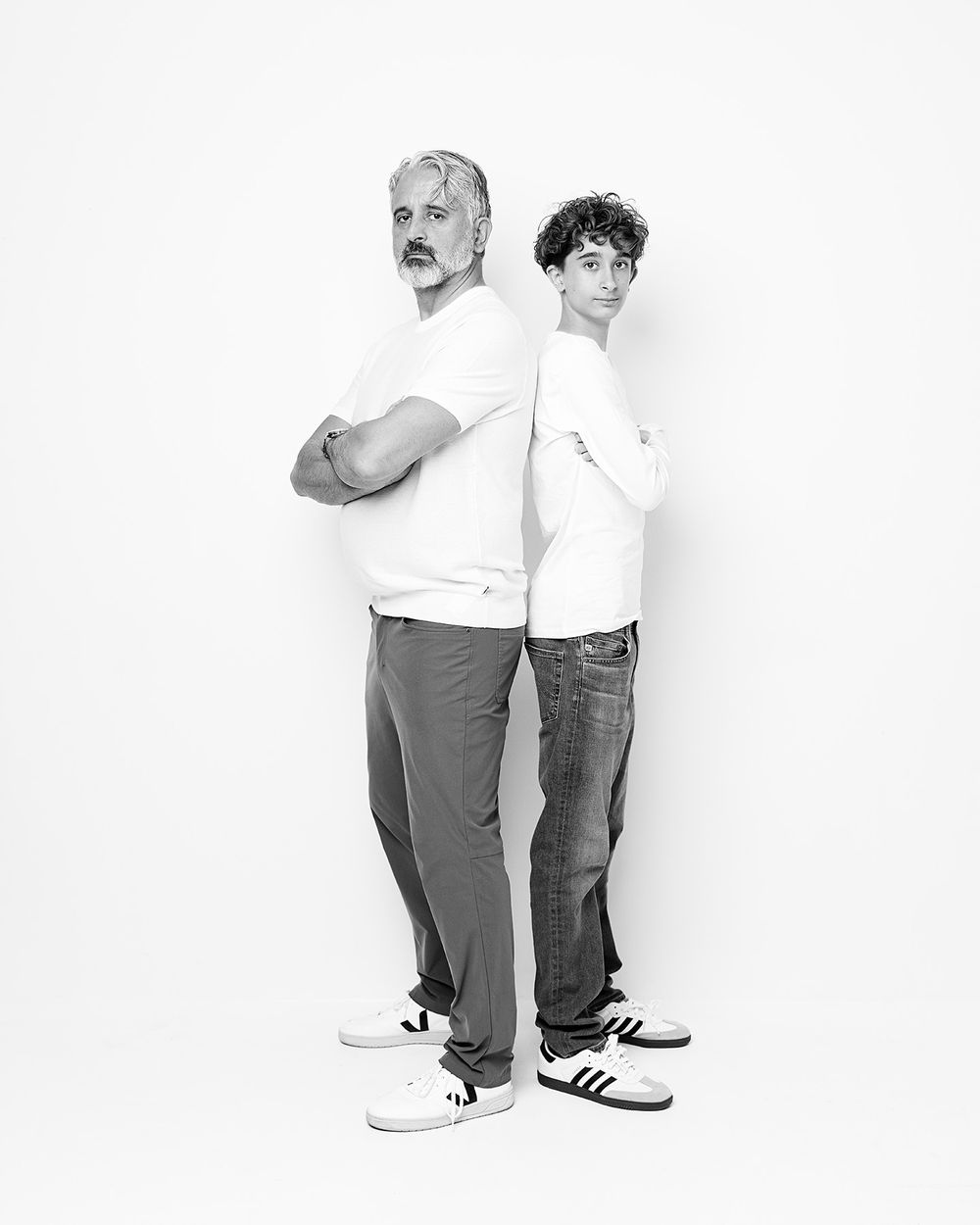 Black and white photo showing two people in casual wear standing back to back against a white background.