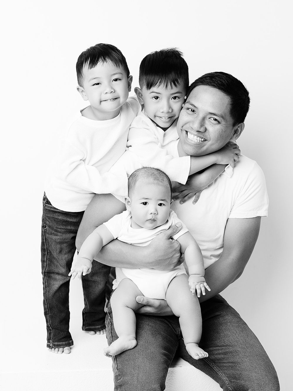 Black and white portrait of a family of four wearing white shirts against a white background.