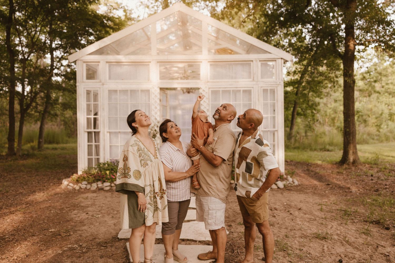 Family sharing joyful moment outside white greenhouse structure in woodland setting.