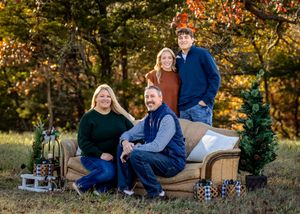 Family group sitting together on a blanket outdoors during autumn with golden foliage and sunlight in the background.
