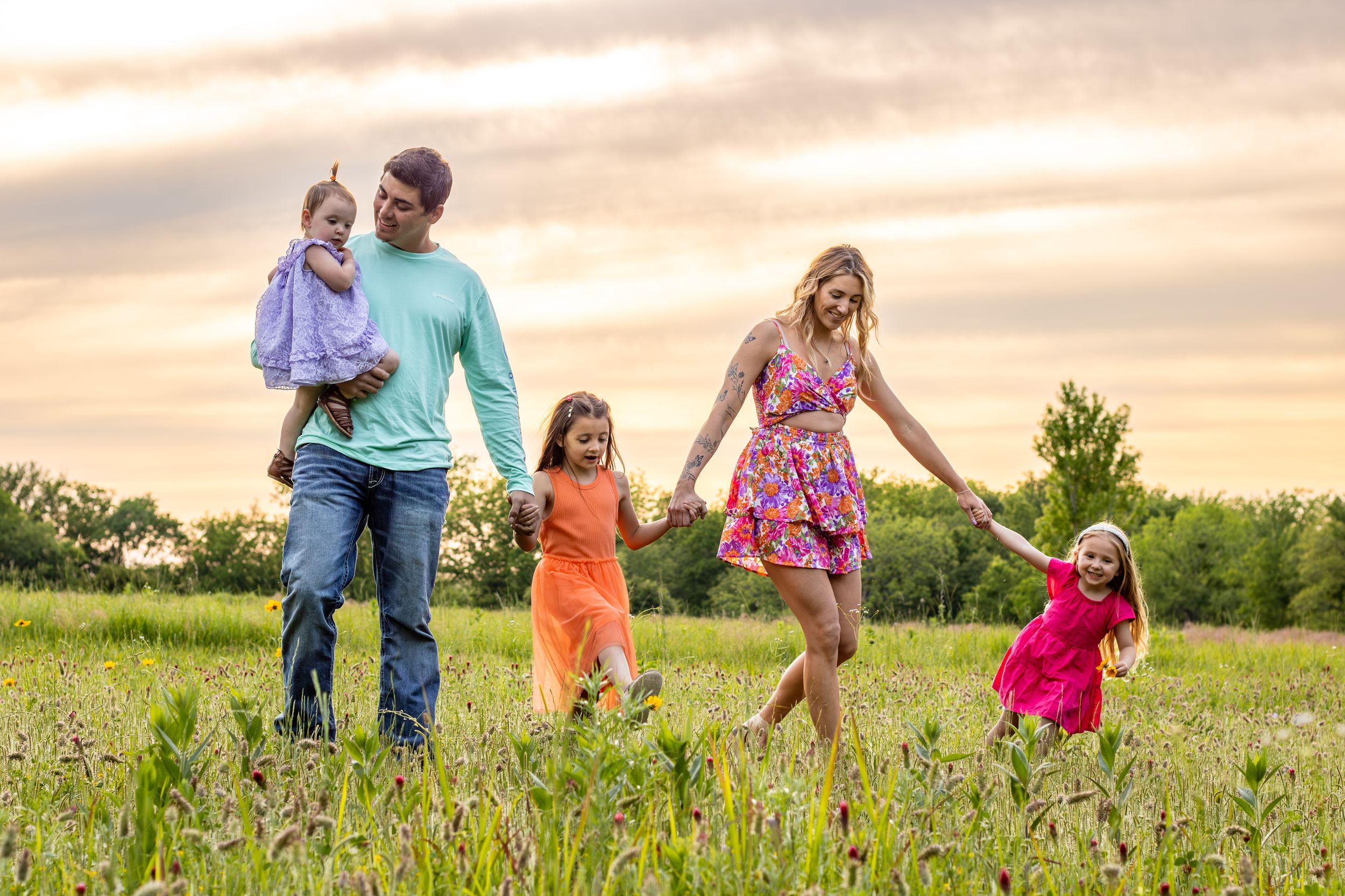 Family walking and playing together in a flower field during golden hour sunset lighting.