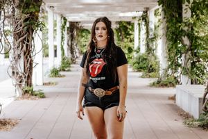 Someone stands in a peaceful garden corridor wearing a Rolling Stones t-shirt and denim shorts.