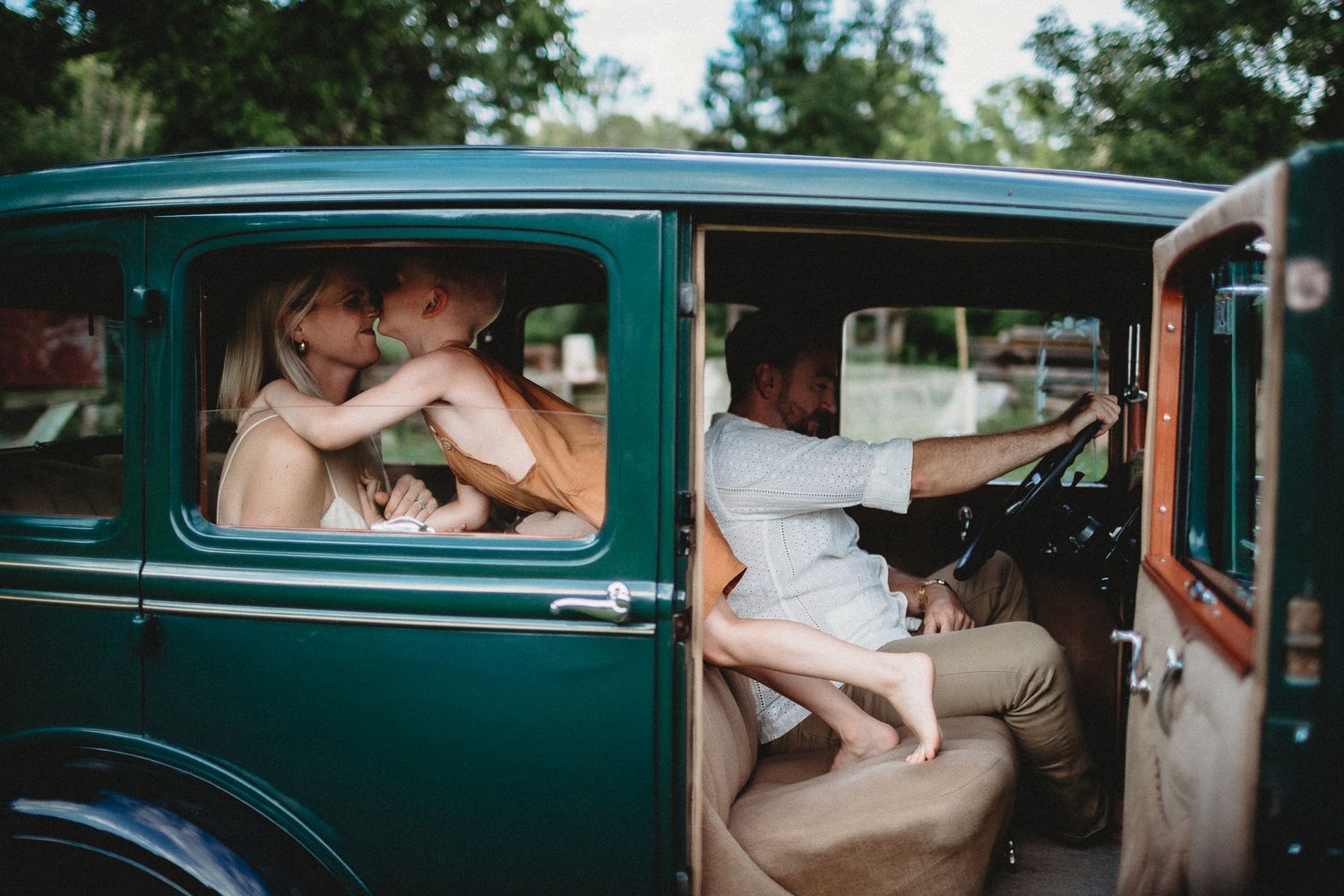 Vintage teal car captures romantic moments of newlyweds through window frames.