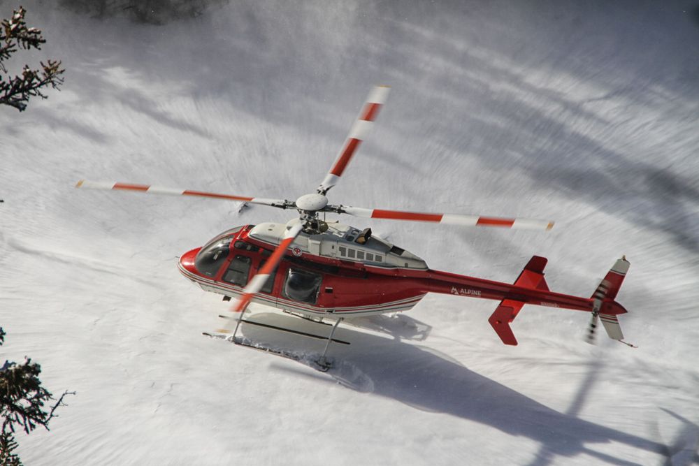 A red and white rescue helicopter flies low over a snow-covered mountain slope.