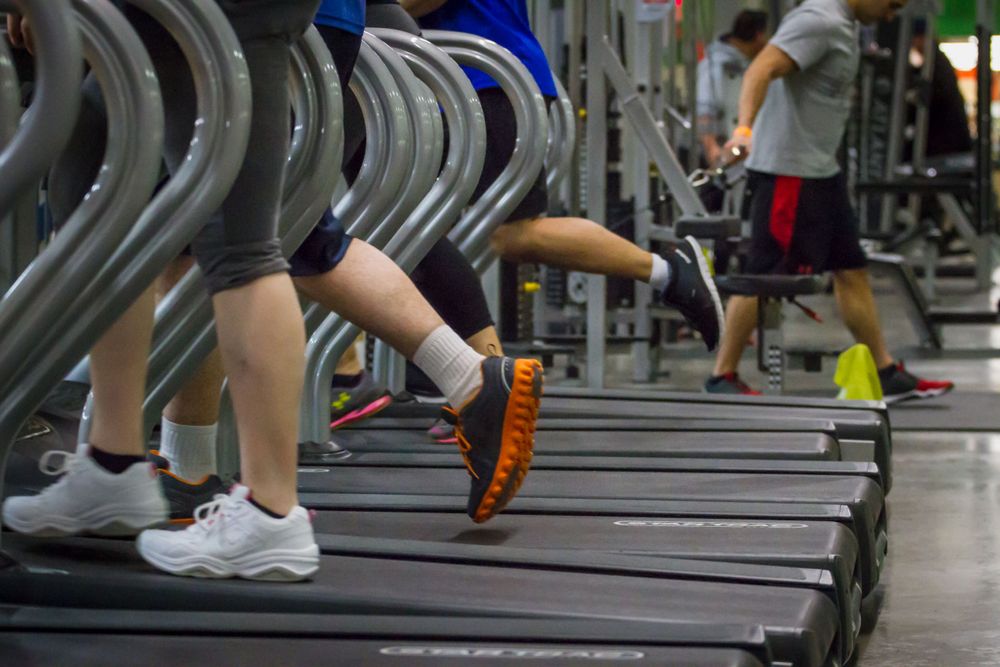 People running on treadmills in a busy gym, close-up of legs and sneakers.