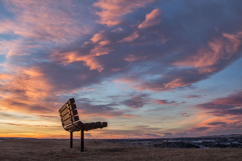 Lone park bench silhouetted against a vibrant pink and purple sunset sky.