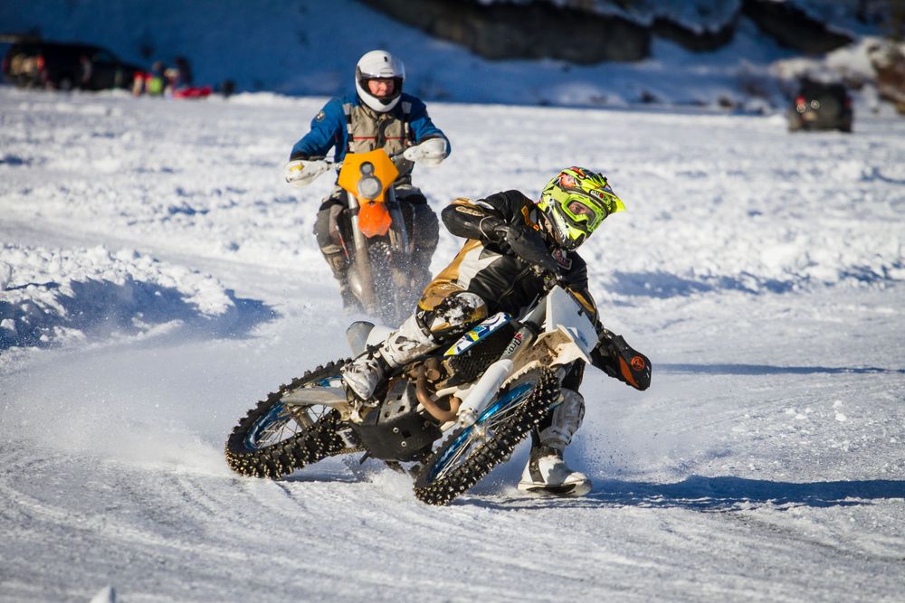 Two motocross riders race dirt bikes through a snowy track in winter competition.