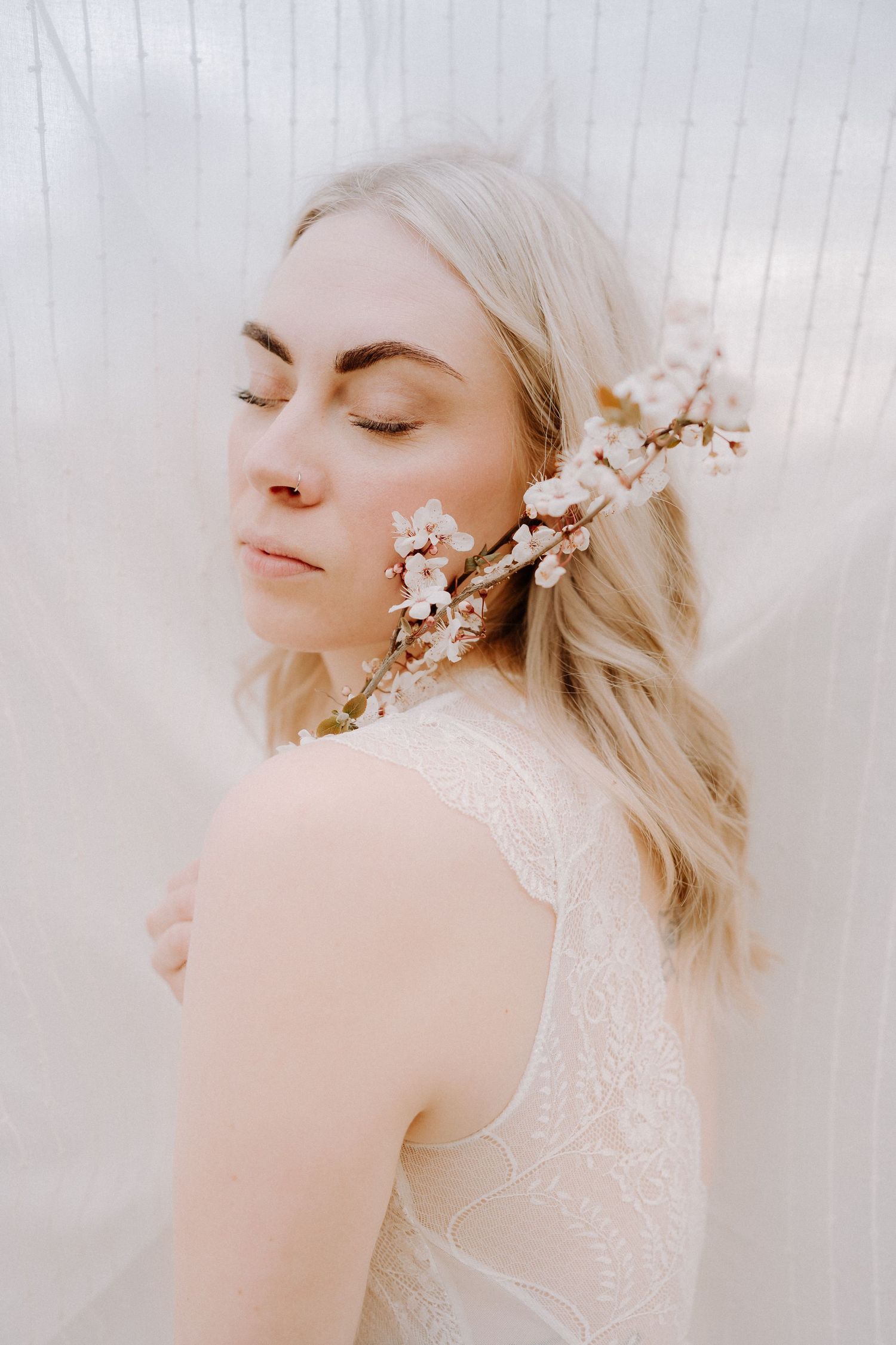 Ethereal bridal portrait with cherry blossoms against soft white background.