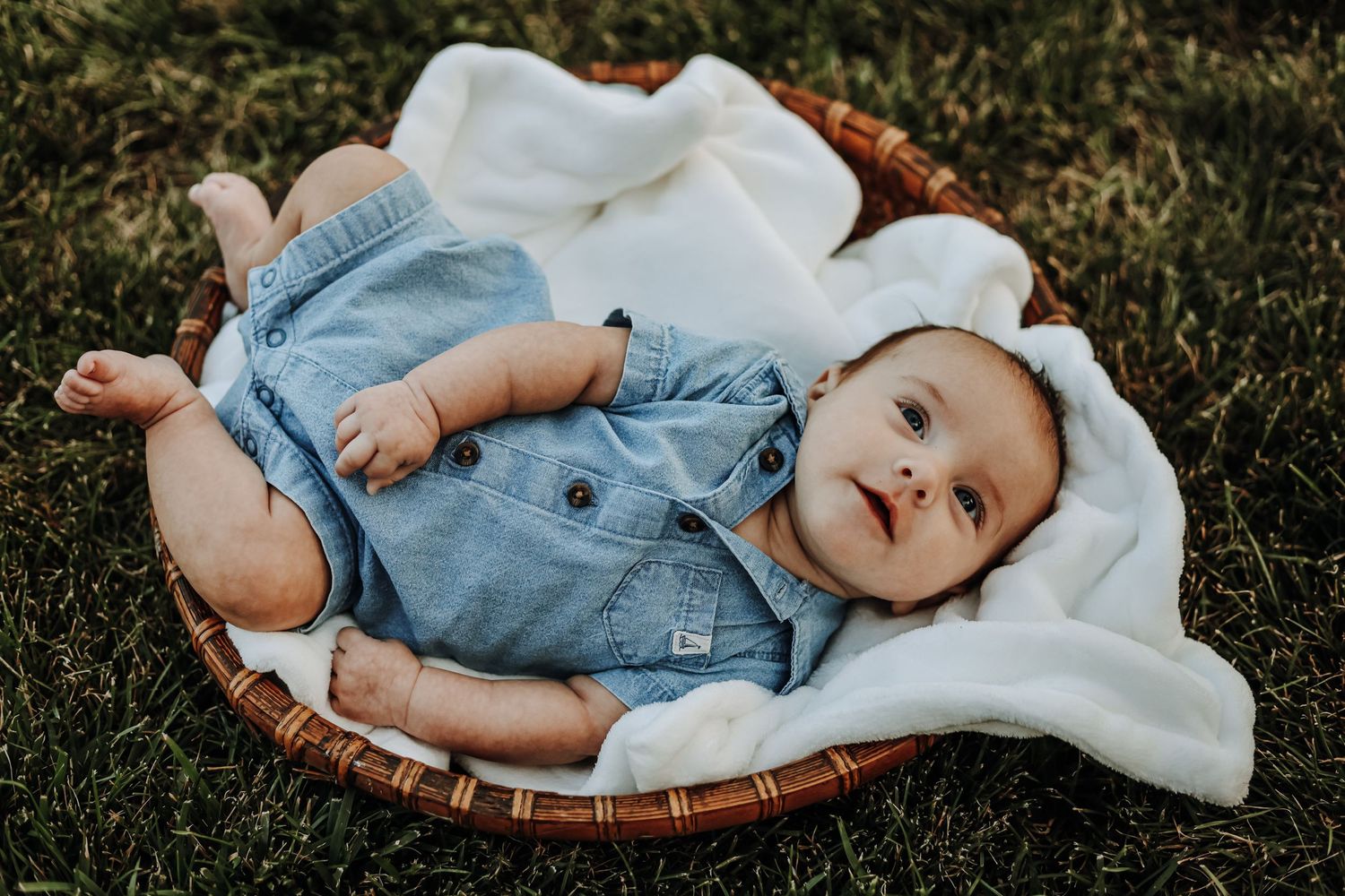 Baby in denim outfit lying on blanket during outdoor photo session. Milestone photography