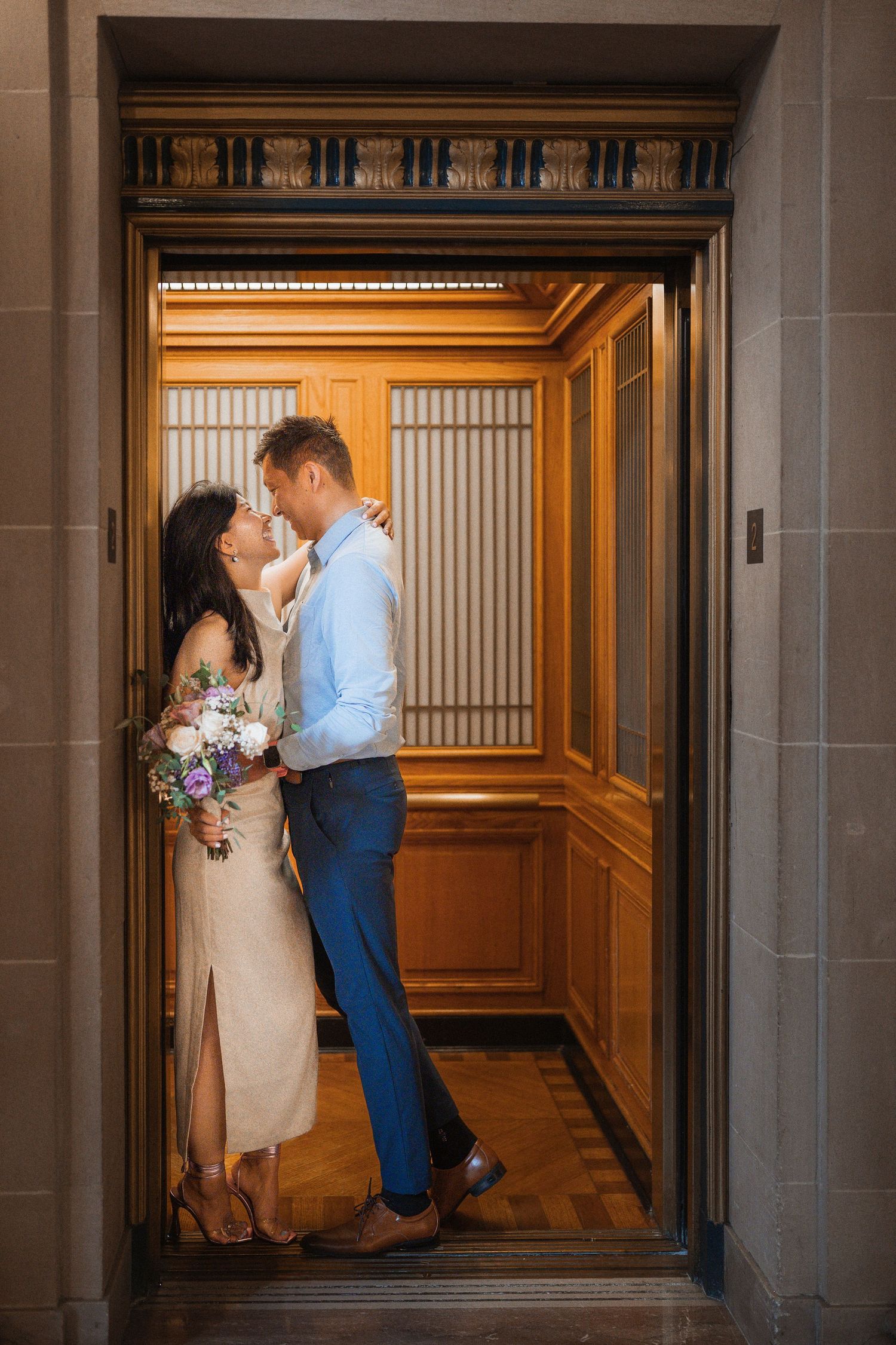 Romantic couple embraces in elegant hallway at City Hall, surrounded by ornate architectural details.