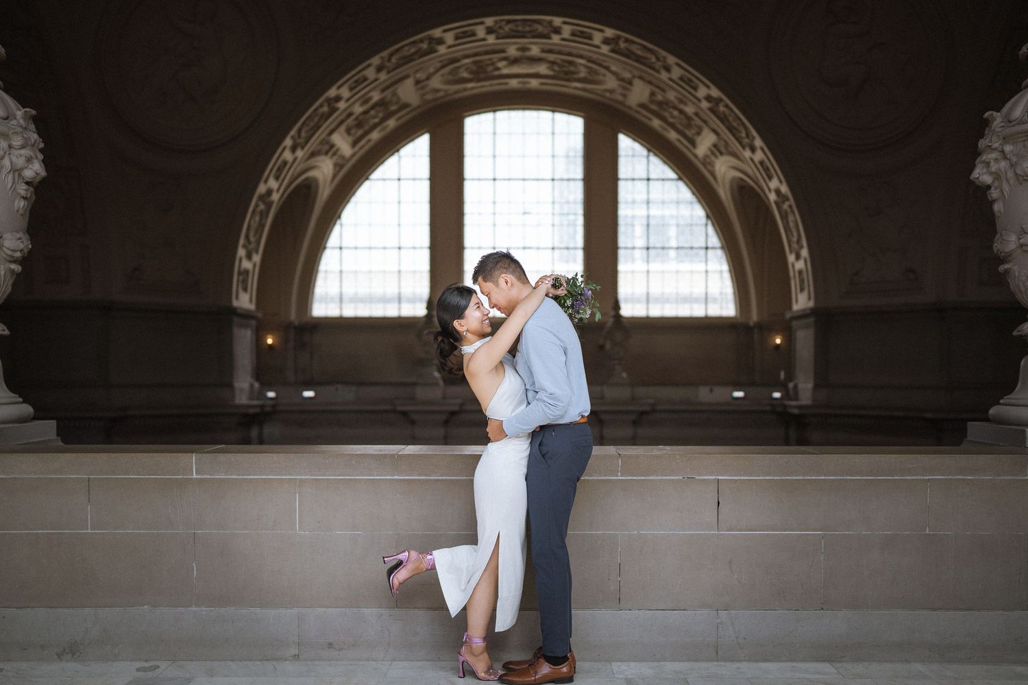 Romantic couple dances in historic building with arched windows and dramatic lighting.