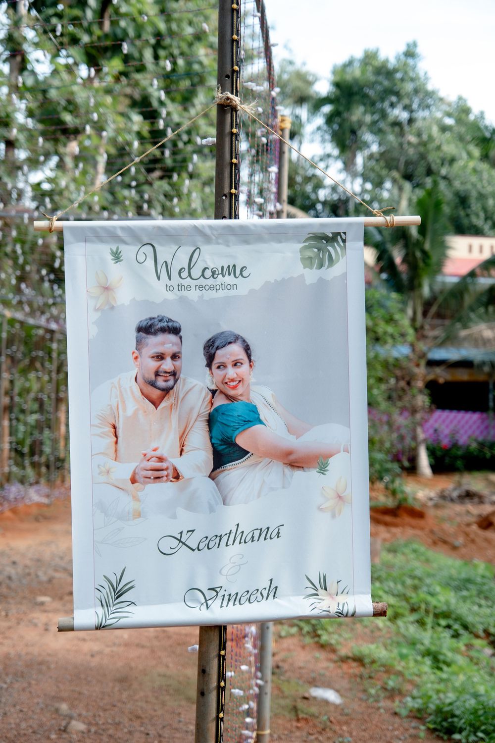 Welcome banner with floral design hanging outdoors during a wedding celebration.