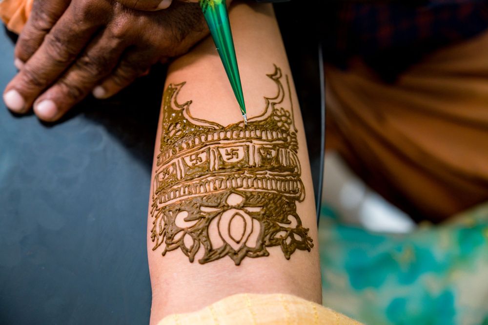 Close-up of detailed henna mehndi art being applied on someone's forearm.