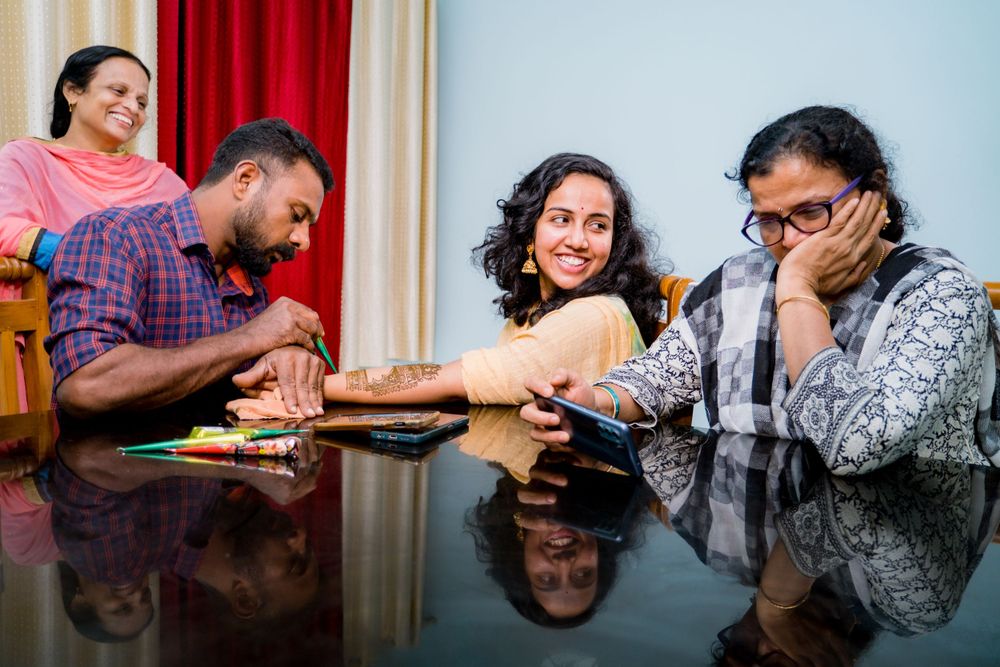 People gathered around a table watching and reacting during a mehndi ceremony.