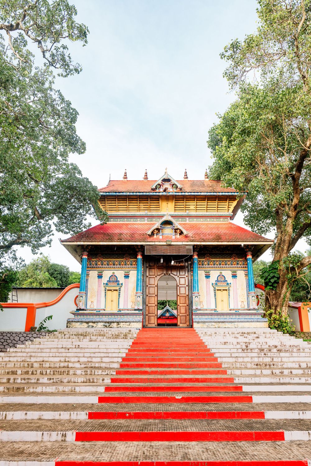 Traditional Kerala temple with red stairs and ornate architecture against blue sky.
