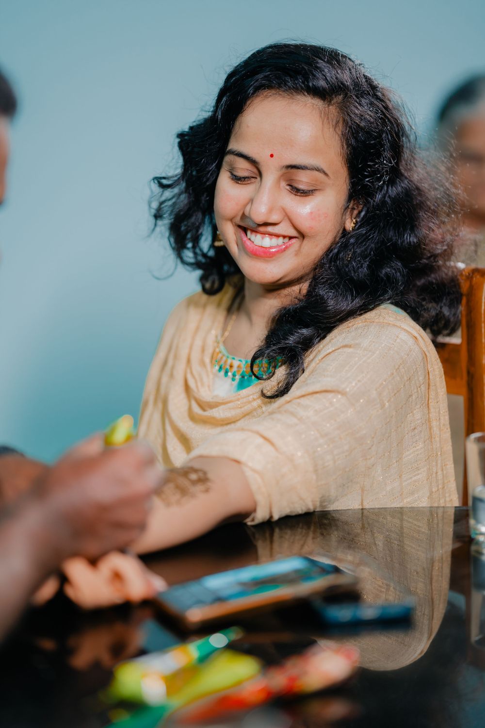 A smiling person in a beige outfit with curly dark hair enjoys a casual moment.