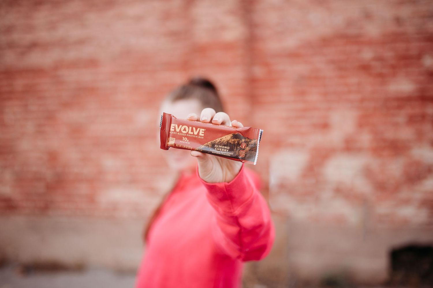 Hand holding up a Focus coffee bottle against a red brick wall background.