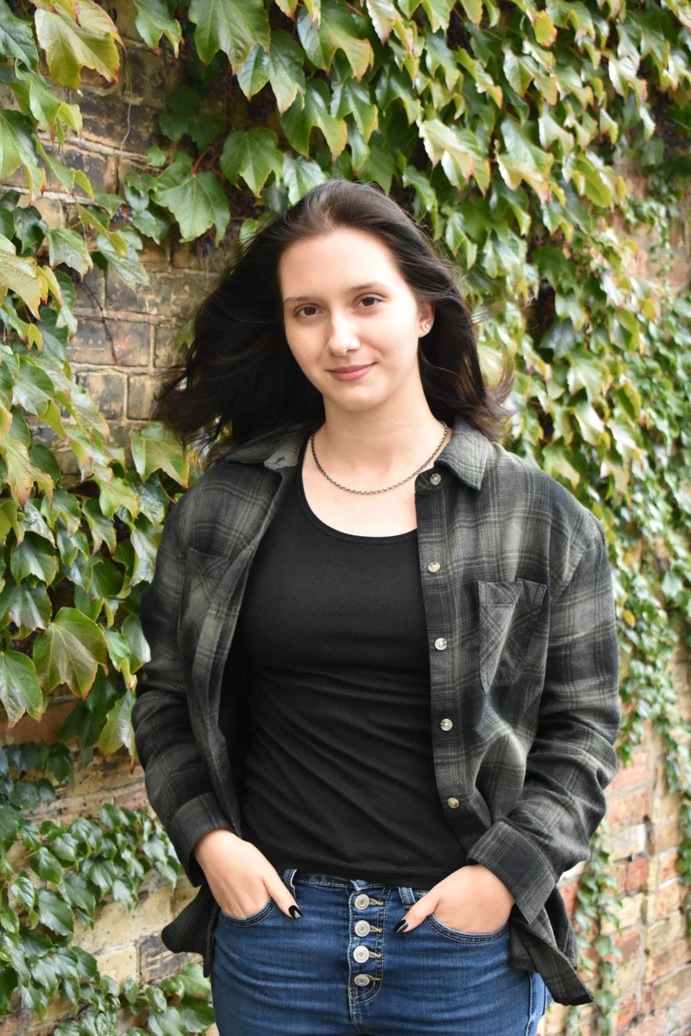 Casual street style portrait against ivy-covered brick wall background.