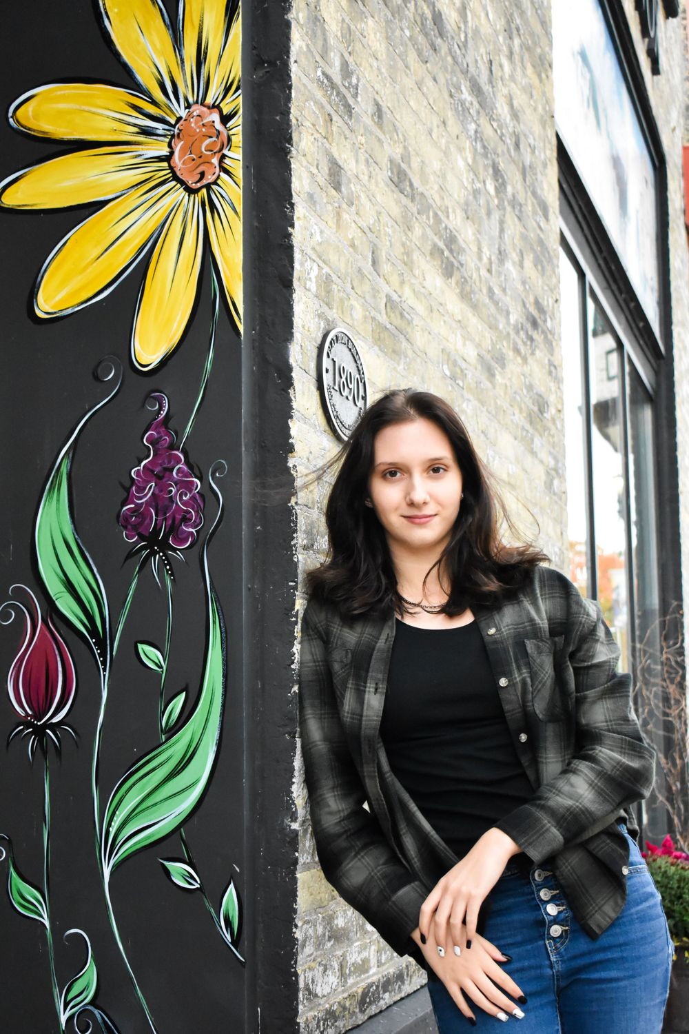Portrait beside colorful floral mural featuring sunflower and botanical designs.