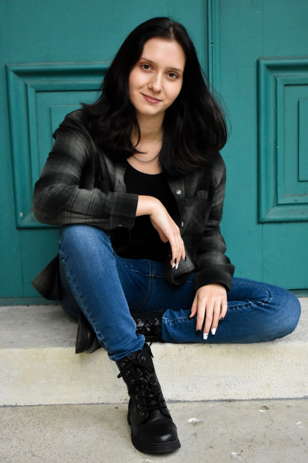 Urban casual portrait featuring dark plaid shirt and combat boots against a turquoise door background.