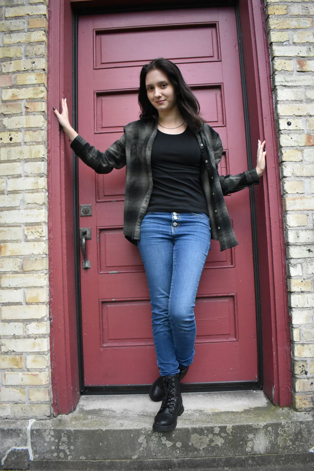 Stylish outfit with plaid jacket and jeans posed against a burgundy door and brick wall.