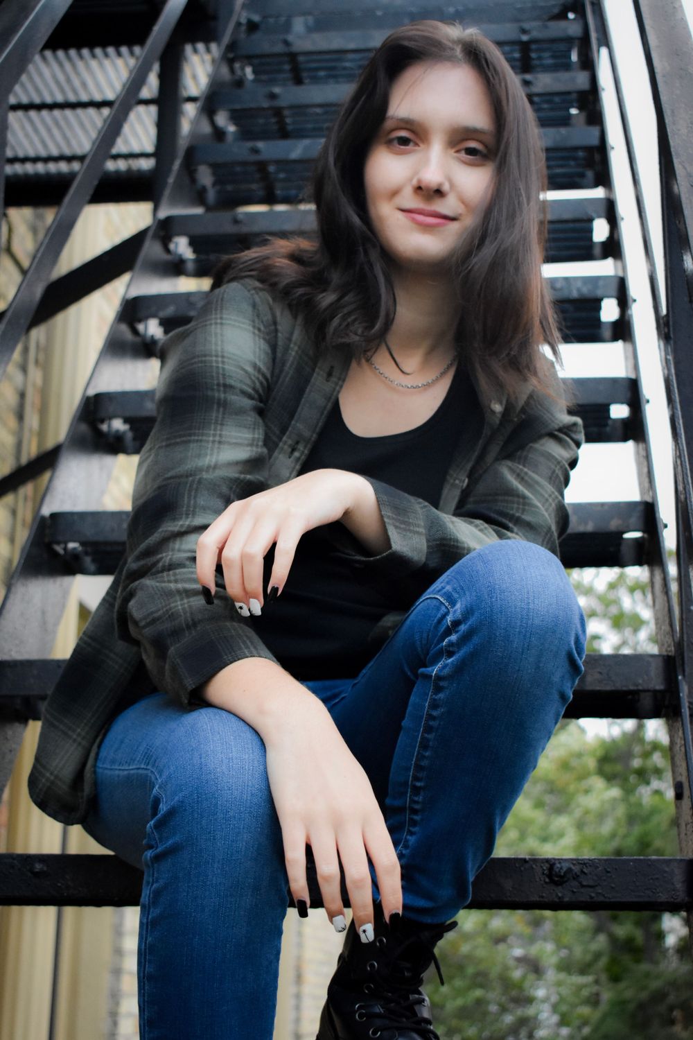 Portrait on metal staircase wearing plaid jacket and jeans in urban setting.