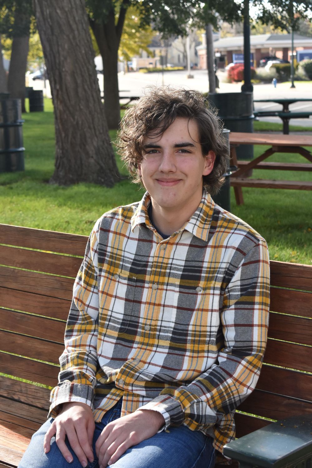 Casual outdoor portrait on park bench wearing plaid shirt on sunny day.