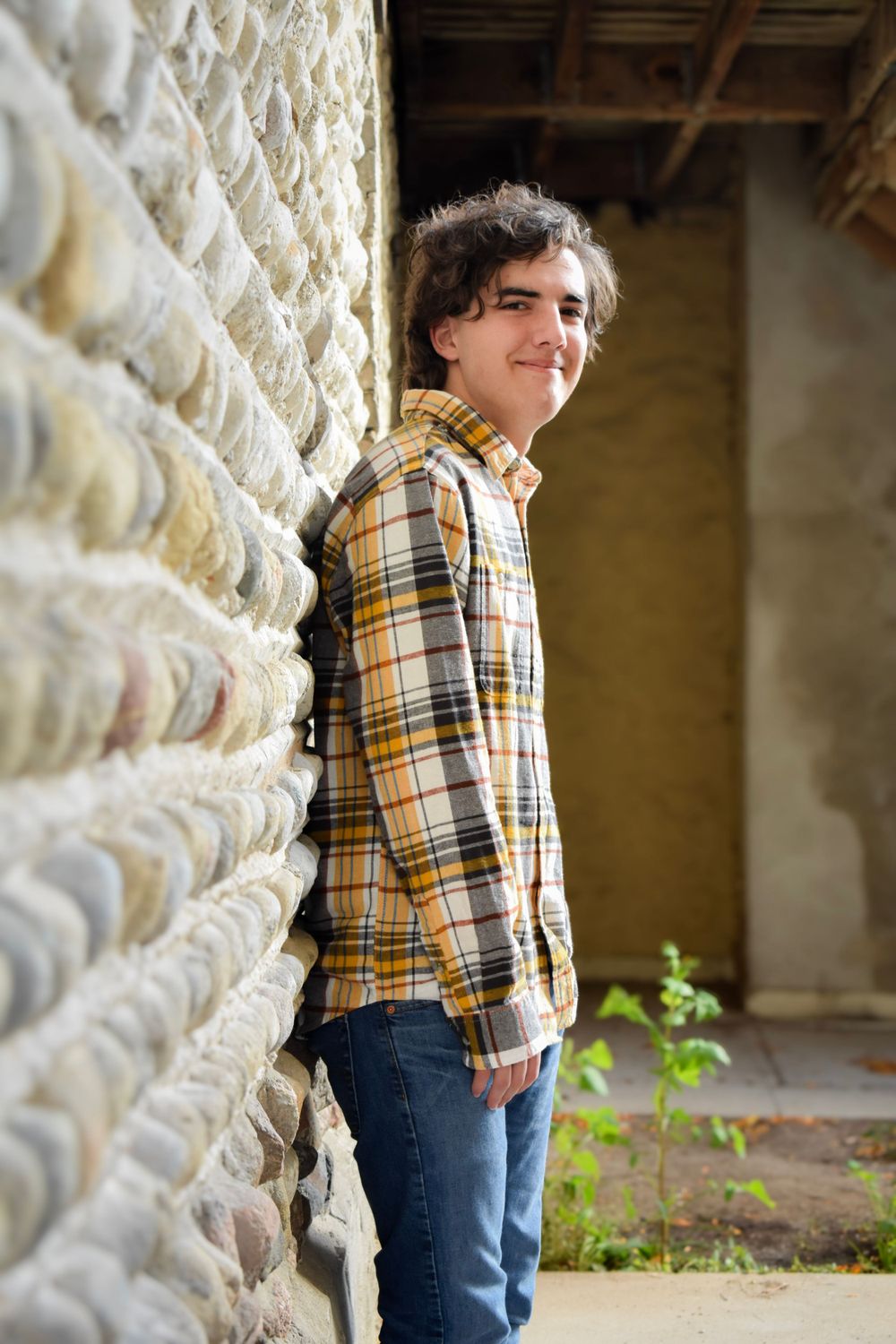 Person in yellow plaid flannel shirt leaning against textured stone wall.