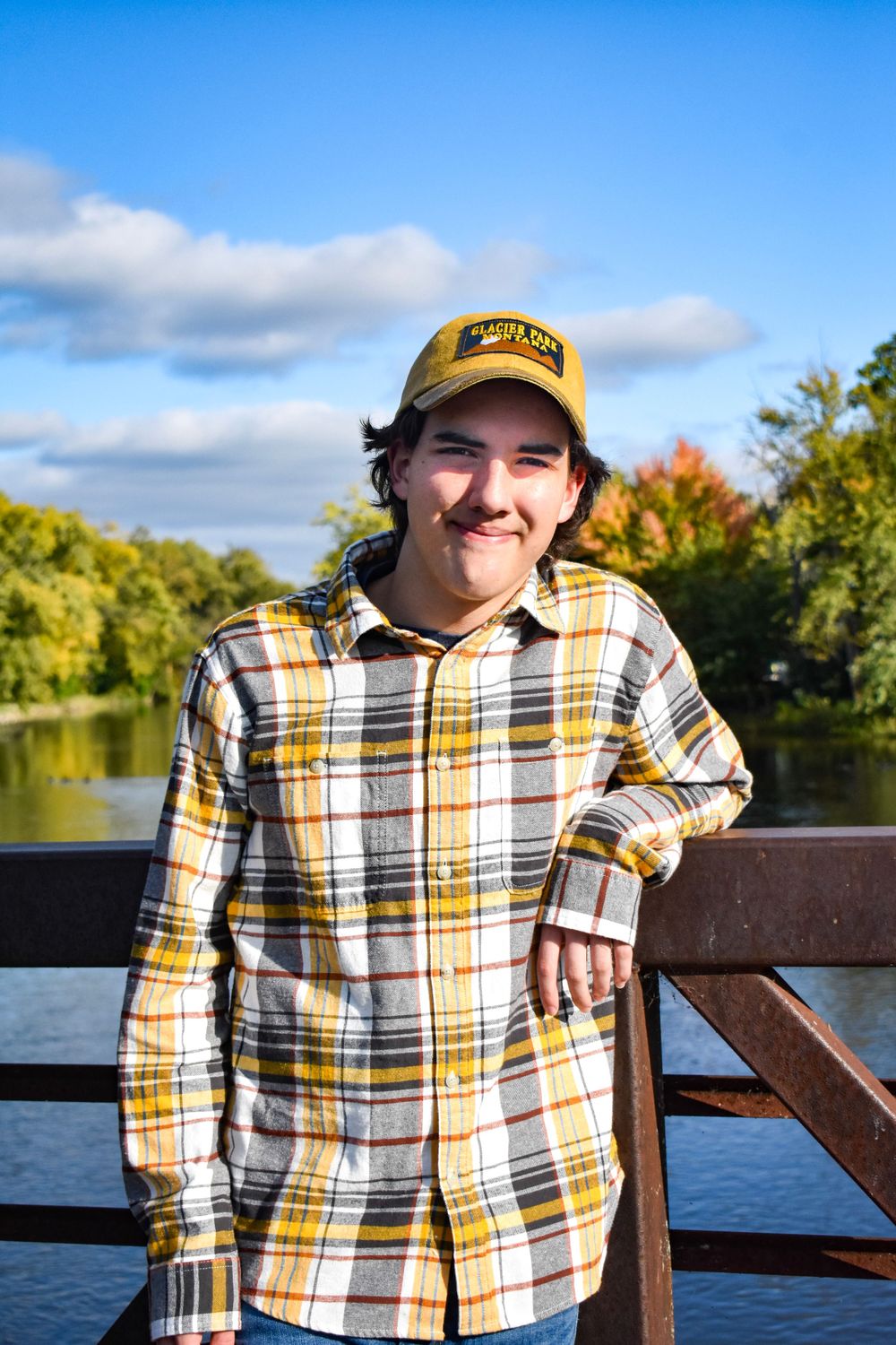 Person wearing baseball cap and plaid shirt smiling by lake on autumn day.