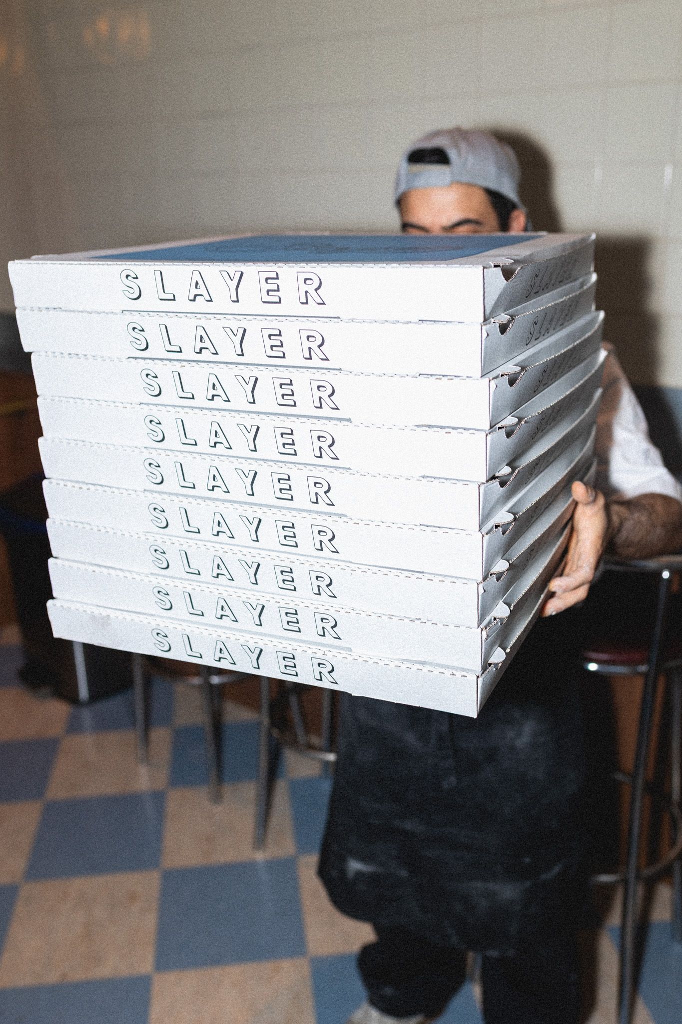 Stack of white pizza delivery boxes labeled 'Slayer' being carried through a restaurant.