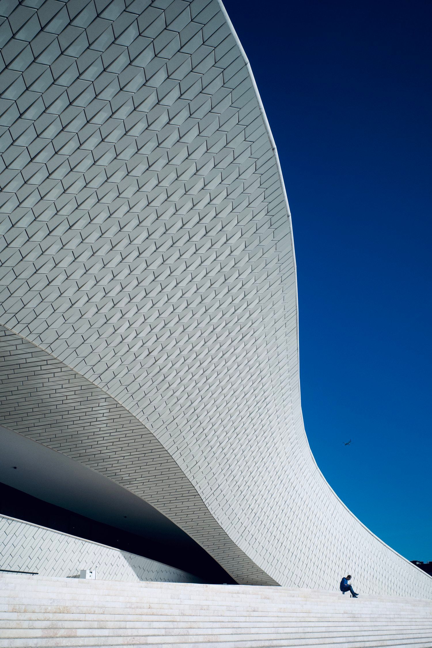 Modern white architectural structure with geometric patterns against deep blue sky.