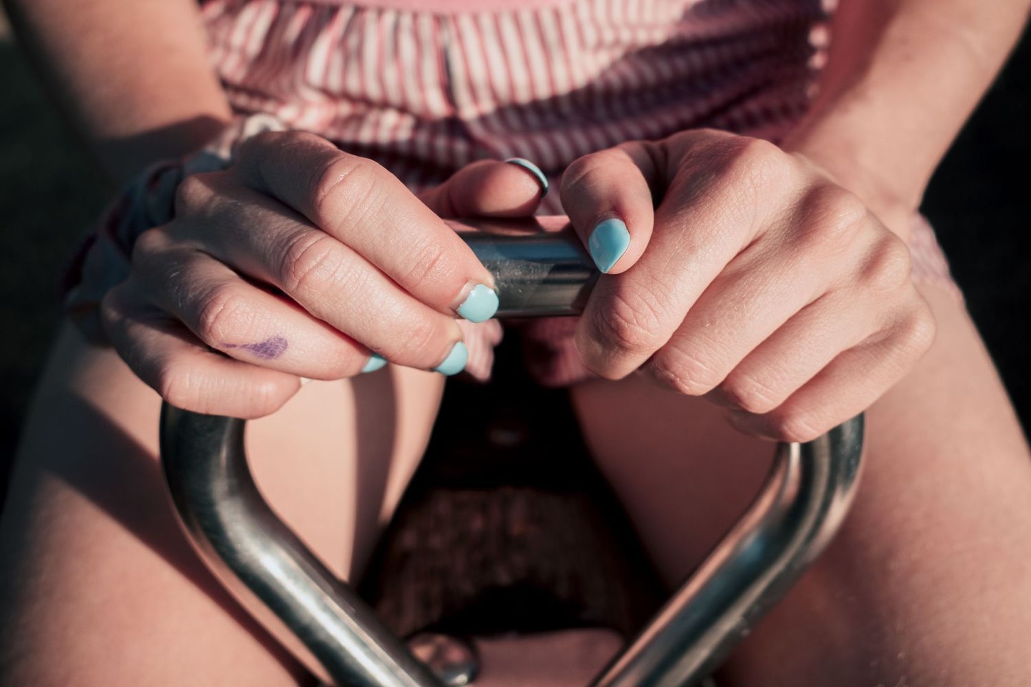 Close-up of hands with blue nail polish using a smartphone, seated outdoors in natural light.