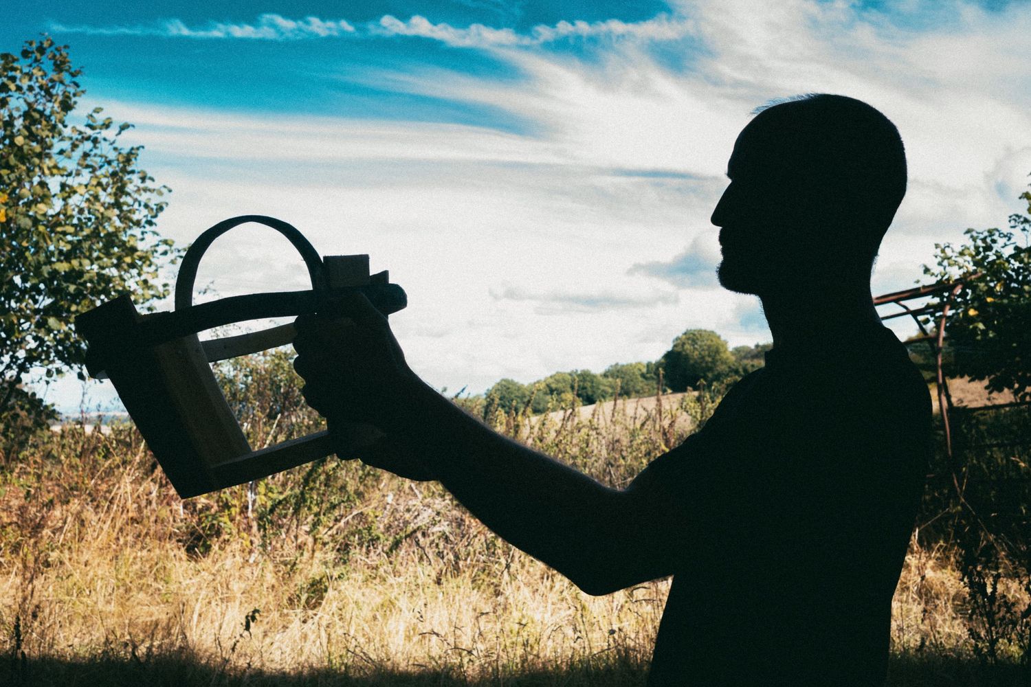 Silhouette of a man holding a watering can against a scenic rural landscape with blue sky and clouds.