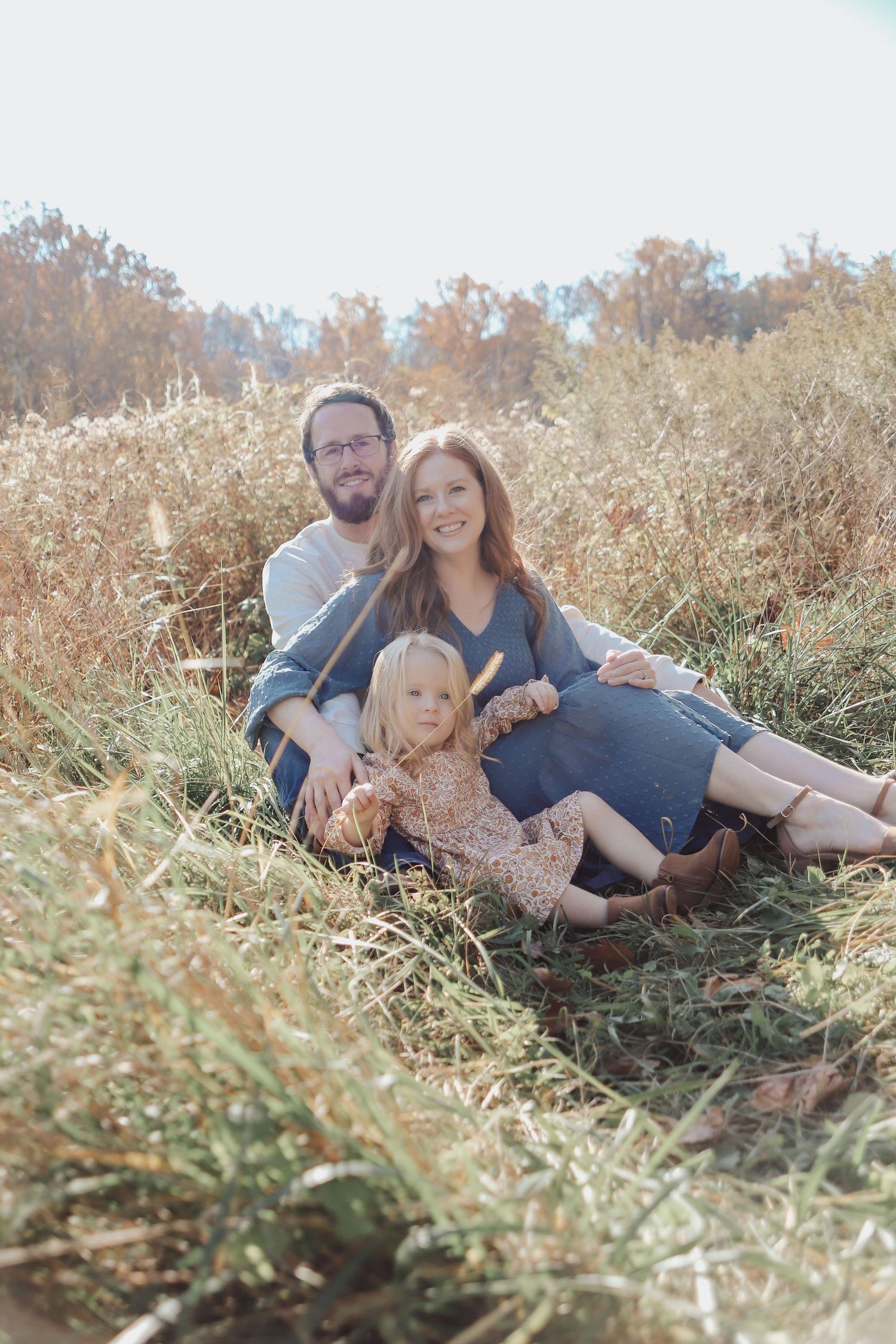 A family relaxes together in a sunlit field with their baby.