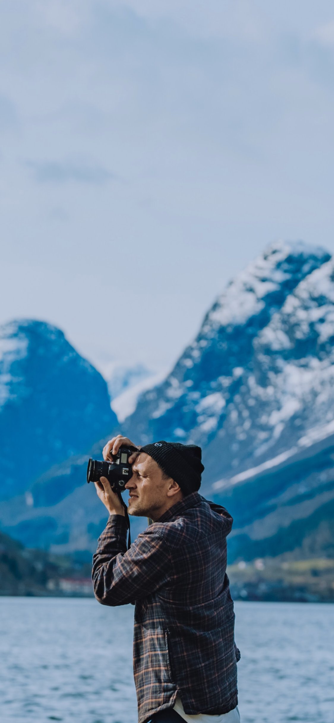 Photographer taking pictures of snow-capped mountains beside scenic lake.