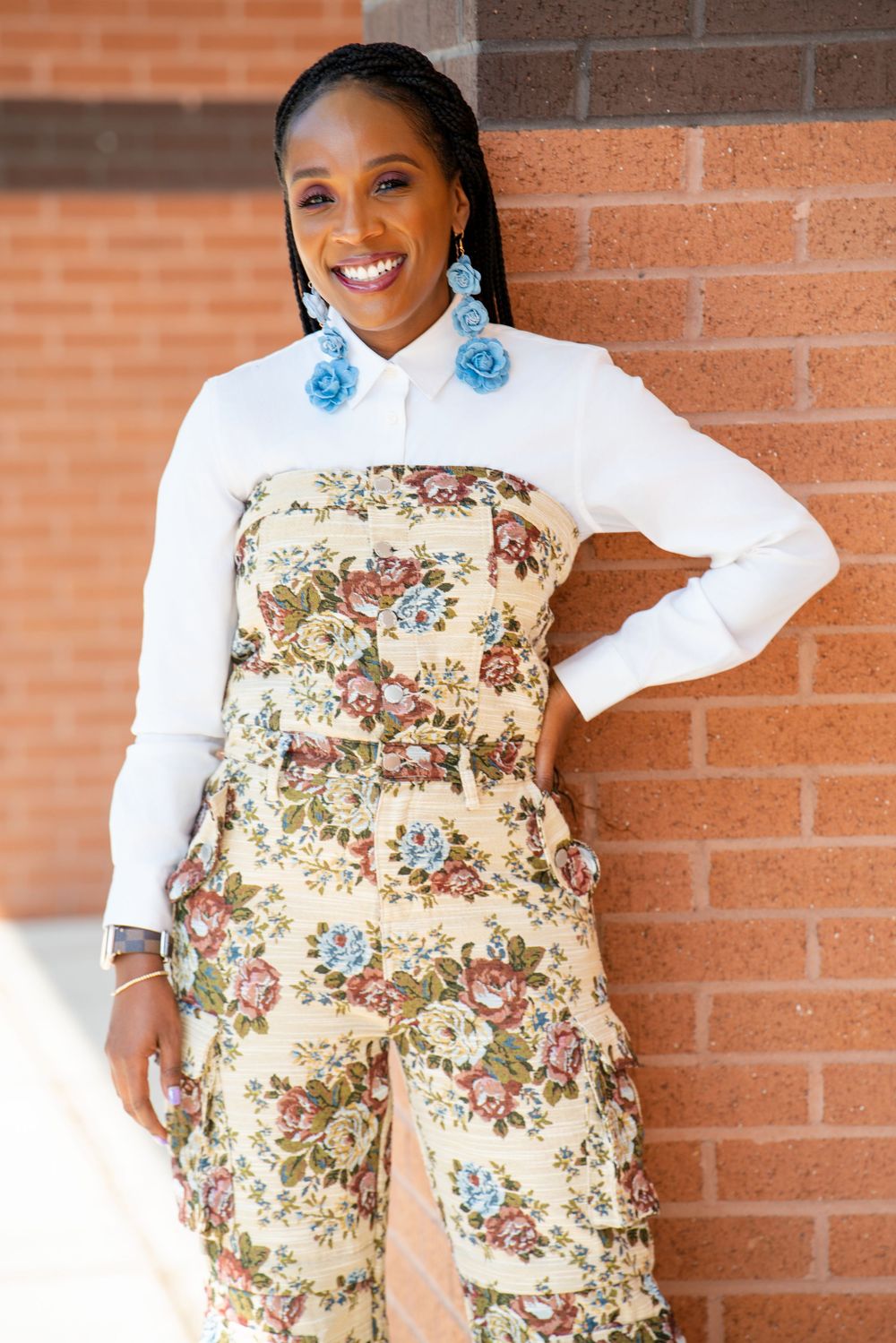 A person wearing a white top and floral print pants poses against a brick wall in four different poses.
