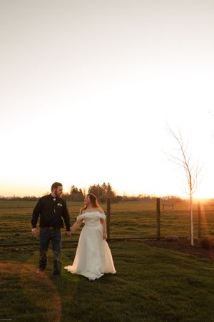 Couple walking through a grassy field at sunset with wooden fence posts.