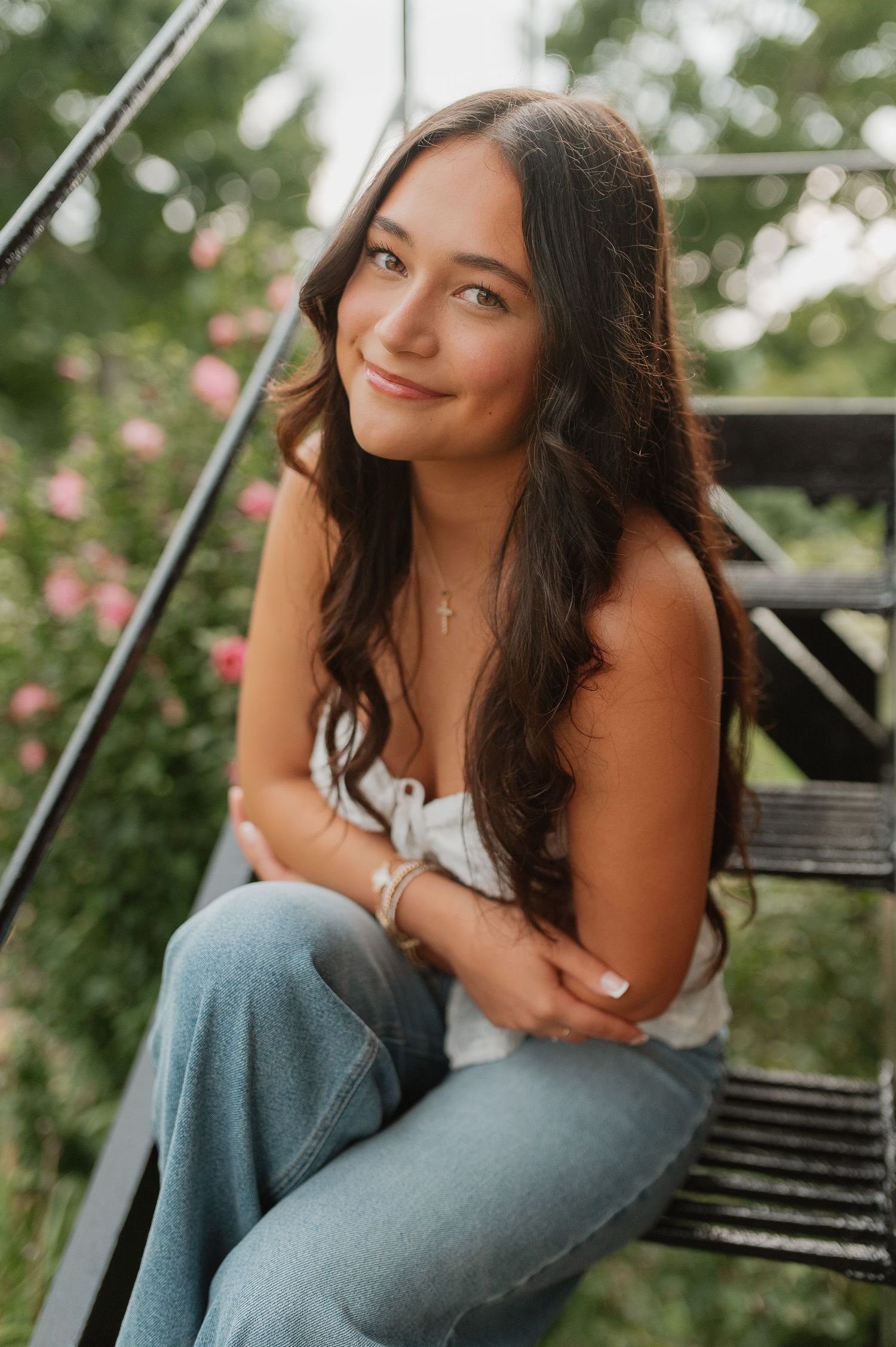 A portrait of someone sitting on outdoor steps wearing jeans and a white top in a garden setting.