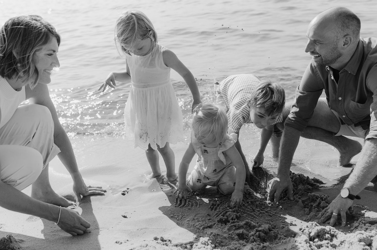 Black and white beach scene of family playing together in the sand.