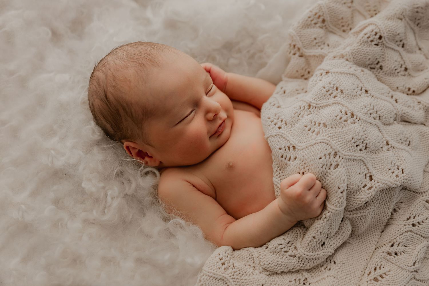 Sleeping newborn baby wrapped in soft neutral knitted blanket during professional photo session. Whakatane Newborn Photographer